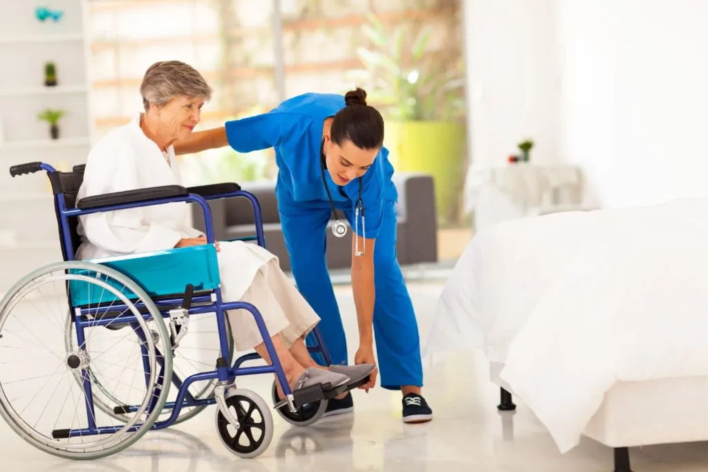 Carer helping an older woman put on her shoes as part of personal care at home in Kent