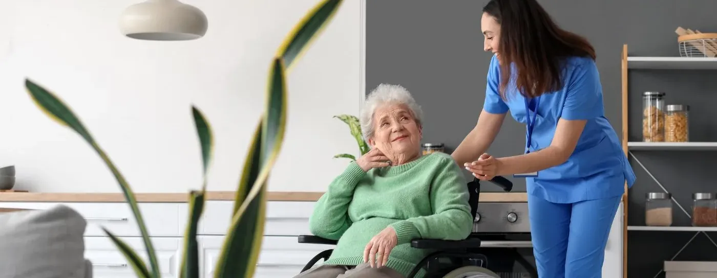 Carer supporting an older woman in a wheelchair during a domiciliary care visit at home in Dartford