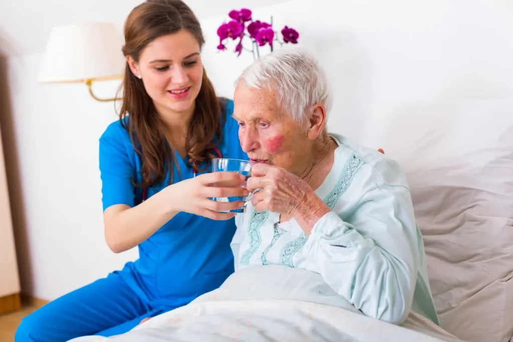 Home carer helping an elderly woman with a drink during a domiciliary care visit in Dartford